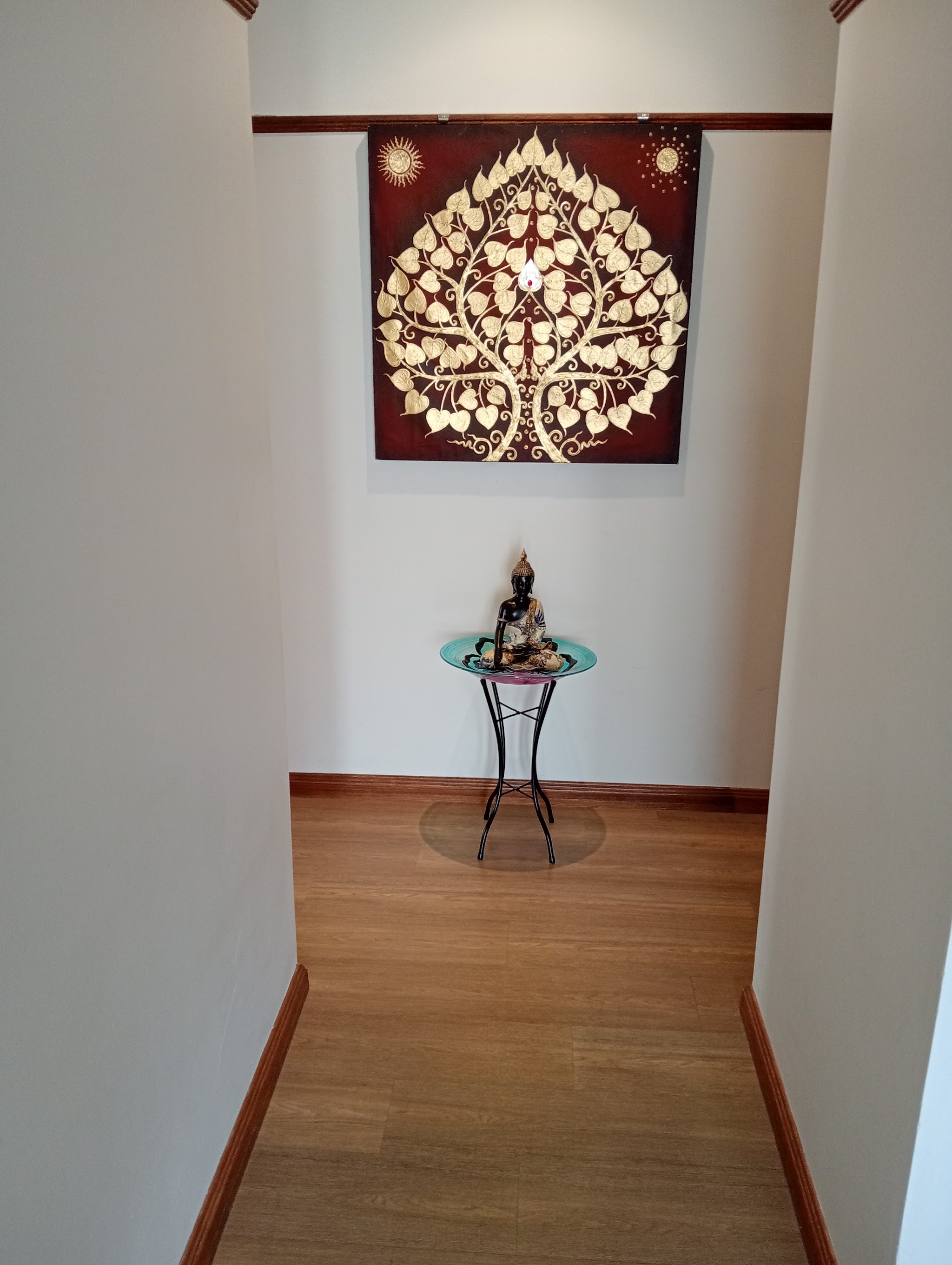 Hallway shrine with a gold Bodhi tree panel and a seated Buddha on a turquoise stand